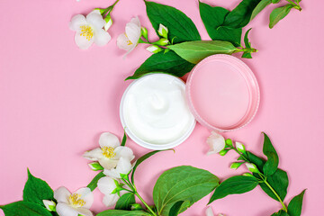Obraz na płótnie Canvas Top view of white plastic cosmetic container for moisturizing cream as a mock up with bright fresh jasmine flowers on pink background with copy space. Body and skin care and beauty concept.