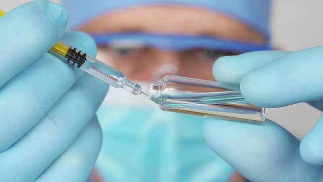 Vaccination. Doctor in the medic face mask is preparing an injection. Syringe with a vaccine, medical solute in the hands of the doctor. Close up view