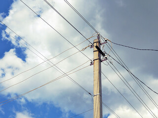 Electric concrete pillar against a blue sky. Illustration on the theme of electricity supply and rising prices. The wires cross against a background of fluffy white clouds. Rural electrification