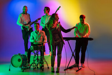 Motion. Young caucasian inspired and expressive musicians, band performing on multicolored background in neon. Concept of music, hobby, festival, art. Joyful artist, colorful, bright portrait.
