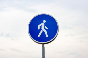 Blue and white round caution road sign for walkway zone and pedestrians.