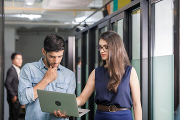 Young businessman holding laptop and walking discusses work with female team, business team of coworkers meeting in creative office