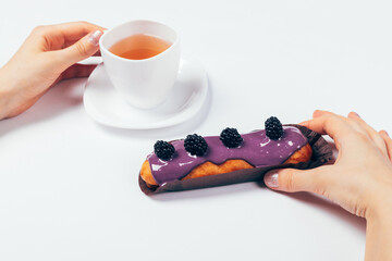 Woman's hands holding cup of tea and delicious eclair cake