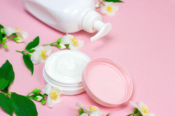Obraz na płótnie Canvas White plastic cosmetic container for moisturizing cream as a mock up with bright fresh jasmine flowers on light pink background with copy space