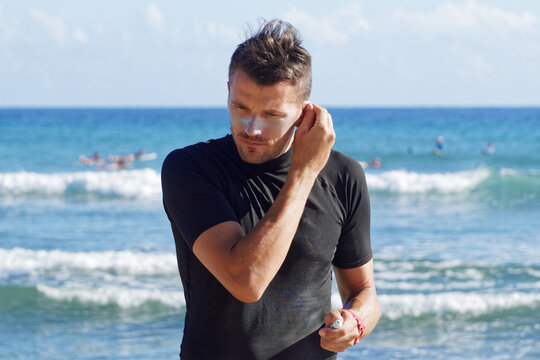 Male Surfer Putting Sunscreen Cream On Ear.