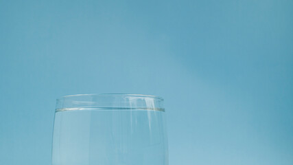  Top of a small glass beaker with clear clean fresh water on a light blue background. The need to drink water. Proper nutrition. Morning habit.