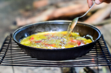 Blur. A spoon stirs fried eggs with vegetables in a pan close-up on an outdoor grill.