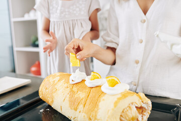 Mother and daughter decorating swiss roll they baked with whipped cream and orange slices