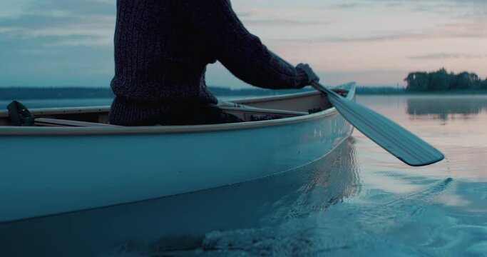 CU view of a paddle, man canoeing alone boat on a large lake at dawn. Shot on RED cinema camera with 2x anamorphic lens