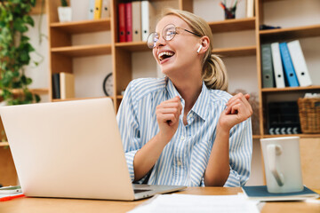 Image of woman using earphones and dancing while working with laptop