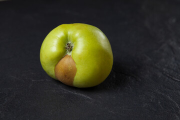 An ugly fruit. Green apple with a spot on a dark background. Concept - Food waste reduction. Using in cooking imperfect products