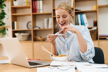 Image of woman taking photo while eating noodles and working with laptop