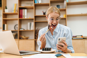 Image of woman eating sushi while using cellphone and laptop
