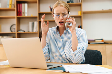 Image of businesswoman talking on cellphone while working with laptop