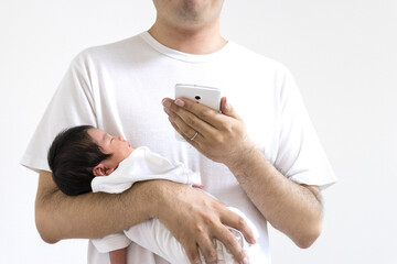 生後18日の赤ちゃんを抱いてスマートフォンを使う30代の男性