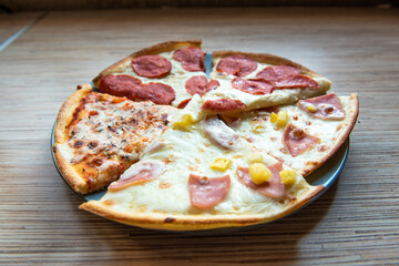 Slices of different pizza with bacon, pepperoni sausages, mushrooms and cheese on a plate and a wooden background
