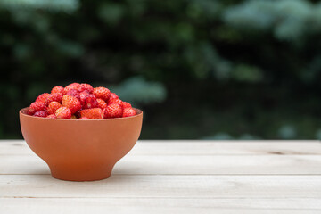 A clay cup with red, juicy strawberries stands on a wooden table