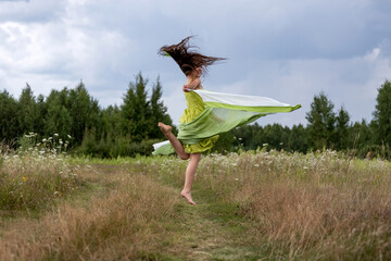 young woman dancing barefoot on the field in a green dress