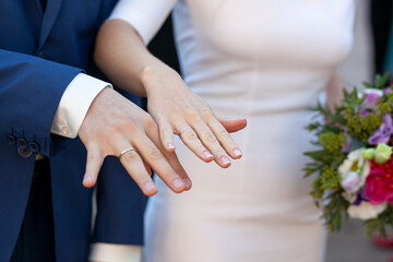 Obraz na płótnie Canvas close-up hands with the apart fingers of the bride and groom showing wedding rings. Bride in a white skin-tight dress, the groom in a blue suit. bridal bouquet