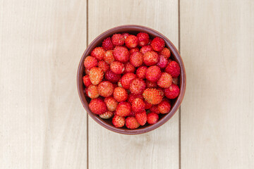A clay cup with red, juicy strawberries stands on a wooden table. View from above
