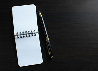 a pen and small daily note on a black table