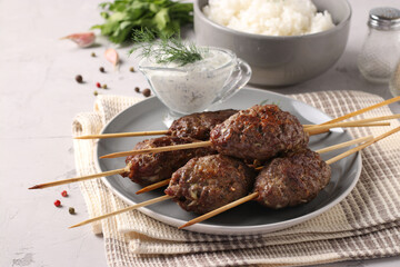 Kofta kebab on wooden skewers on a plate with sauce and a side dish of rice on the table,...