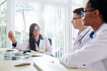 Fototapeta premium Young female medical scientist pointing at computer screen when explaining results of her research to colleague