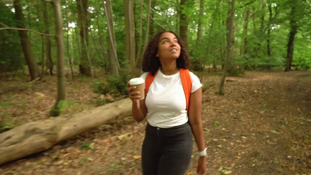 Teenage girl young woman hiking with orange backpack and takeaway coffee cup  in forest woodland 