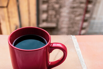 A red cup of fresh black coffee standing on a window sill of an apartment in a French village in the morning