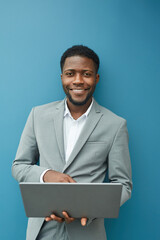 Vertical waist up portrait of contemporary African-American businessman holding laptop and smiling...