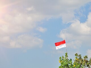 Indonesian flag waving in the wind against a blue sky and clouds. Red and white flag. Independence of Indonesia