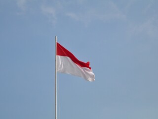 Fototapeta na wymiar Indonesian flag waving in the wind against a blue sky and clouds. Red and white flag. Independence of Indonesia
