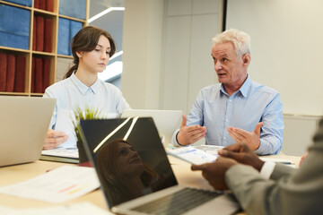 Obraz premium Portrait of white haired mature businessman gesturing actively while talking to employees during meeting in conference room, copy space