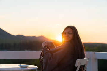 Young woman drinking hot coffee on the balcony with beautiful mountain landscape