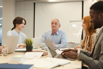 Portrait of white haired mature businessman heading table during meeting with employees in conference room, copy space