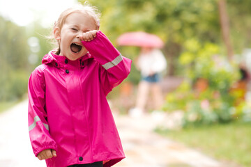 Fototapeta premium Little kid girl screaming standing alone and get lost in park outdoors. Crying baby wearing raincoat.