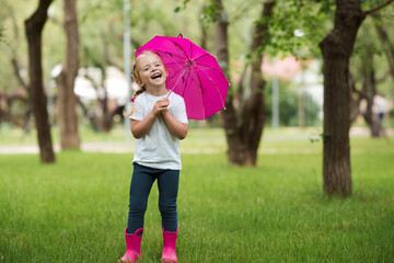 Happy laughing chil girl 2-3 year old wearing waterproof boots and holding pink umbrella posing in...