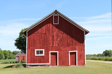 Fototapeta na wymiar a front facing view of a wonderful old red barn with white trim and landscaped lawn with dirt road
