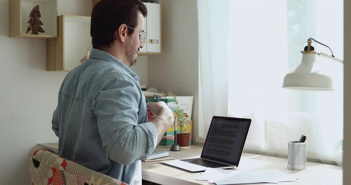 Freelancer sit at table in light room typing using laptop accomplish work relaxing leaned on chair puts hands behind head feels good, side view. No stress, work done, breath fresh air, comfort concept