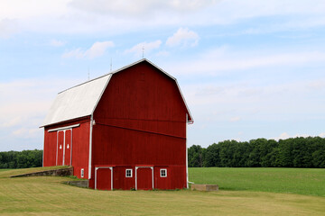 a large white roof red barn with bright white trim and nature loading dock in a natural field with trees and crops beyond