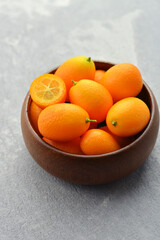 Raw organic kumquat citrus fruits in wooden bowl on concrete background. Healthy vegetarian food. Kumquat fruit cut in half.
