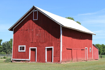 Fototapeta na wymiar a side angle view of a red rural farm barn with white trim and landscaped lawn with bright tin roof