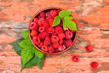 Bowl with ripe raspberries and leaves on wooden backgrounds.