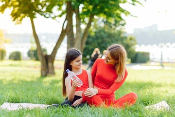 Fototapeta na wymiar A young mother and daughter in sportswear do yoga together in a Park. The concept of a family holiday. Sports, fitness, meditation
