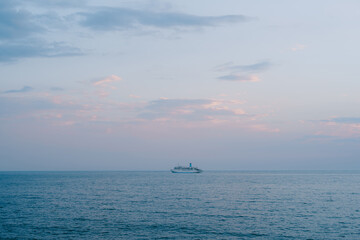 A small cruise liner sails in the open sea against the sunset sky with orange clouds.