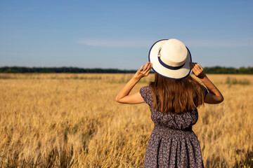 Back of a young girl in white hat looking at a golden wheat field