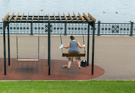 Woman swinging on a swing on the embankment. View from the back. Green grass in summer. Concept of recreation and entertainment without complexes of overweight people.
