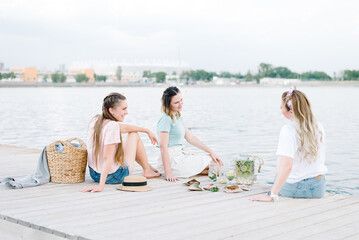 three girls sitting on a wooden pier in front of the water. rest, picnic,lemonade