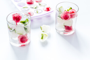 Cocktail glasses with berries in ice cubes on white table