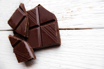 Dark chocolate bar top view mock up with space for text close up. Broken pieces of dark chocolate macro, mock-up for design. Food background over white wooden table.